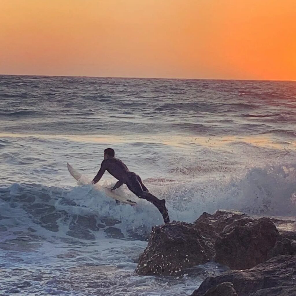Surfer jumps in the sea with surf board at sunset