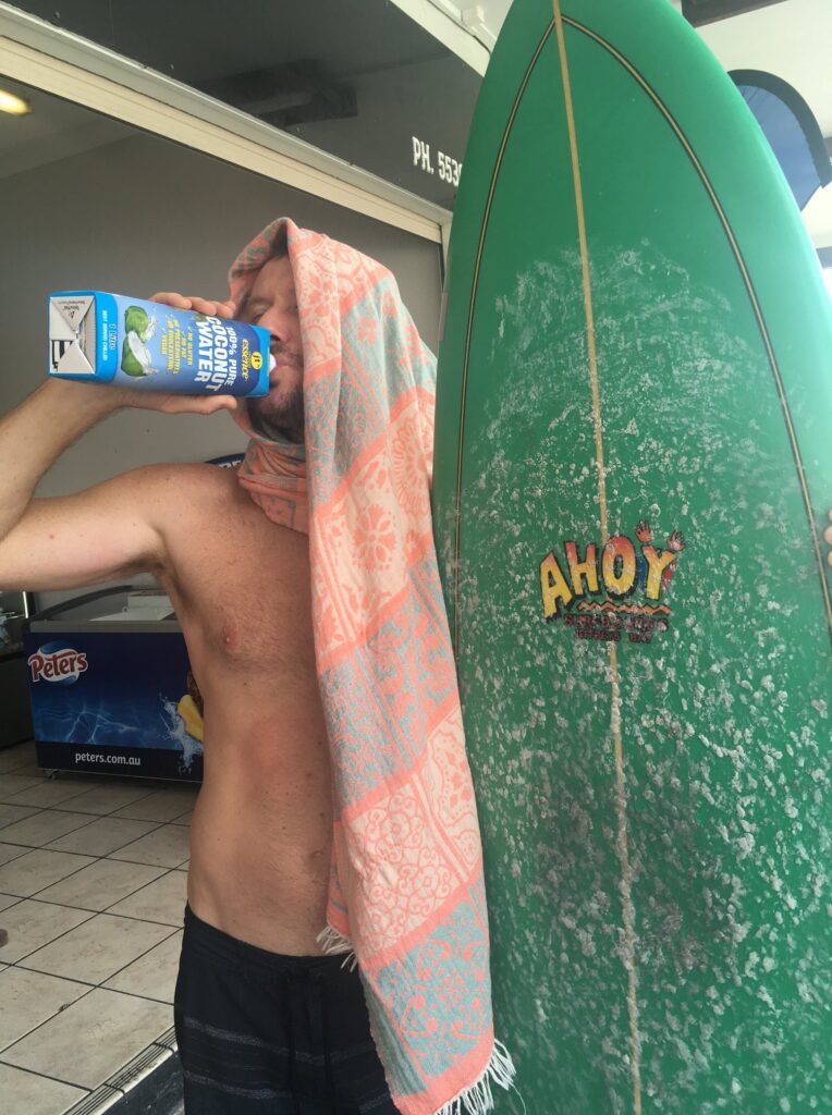 Surfer drinking coconut water out of carton near green surf board