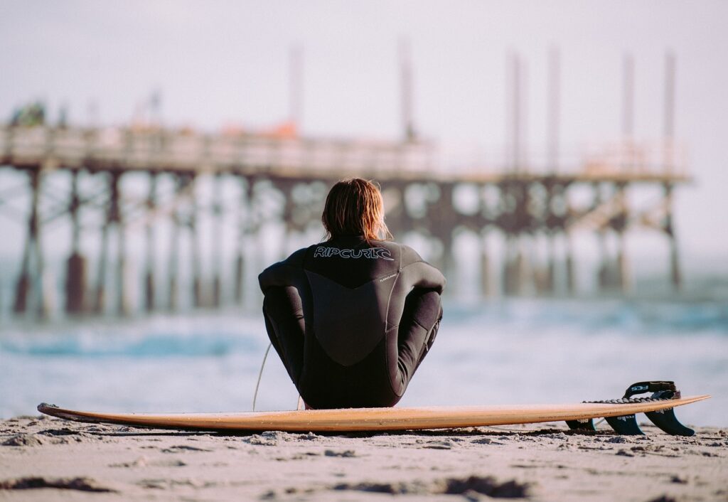 A surfer sitting on his board looking at a pier