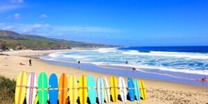 Surfers riding waves on a sunny Cornwall beach.