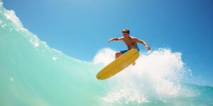 Teen surfer mid-air above a breaking wave, clear sky.