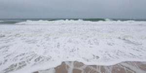 Large waves crash on a sandy beach.