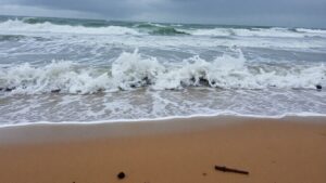 Stormy waves crashing on a beach with debris.