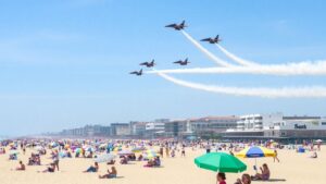 Jets and planes fly over beach crowds and umbrellas.