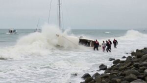 Rescuers save people from capsized sailboat in rough surf.