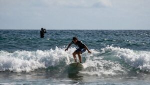 Surfer riding a wave, filmer in background.