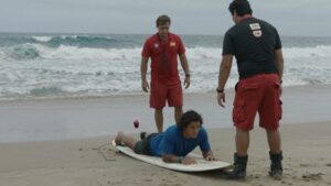 Surfer injured on beach, waves in background.