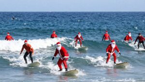 Surfers in Santa suits riding waves at Cocoa Beach.