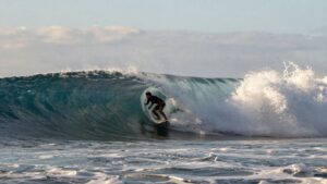 Surfers ride a massive wave at Pipeline during sunset.